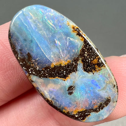 A loose, oval cabochon cut boulder opal stone from Queensland, Australia.