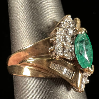 A yellow gold marquise cut emerald and diamond ring.  The diamonds are prong set round cuts and channel set baguette cuts.