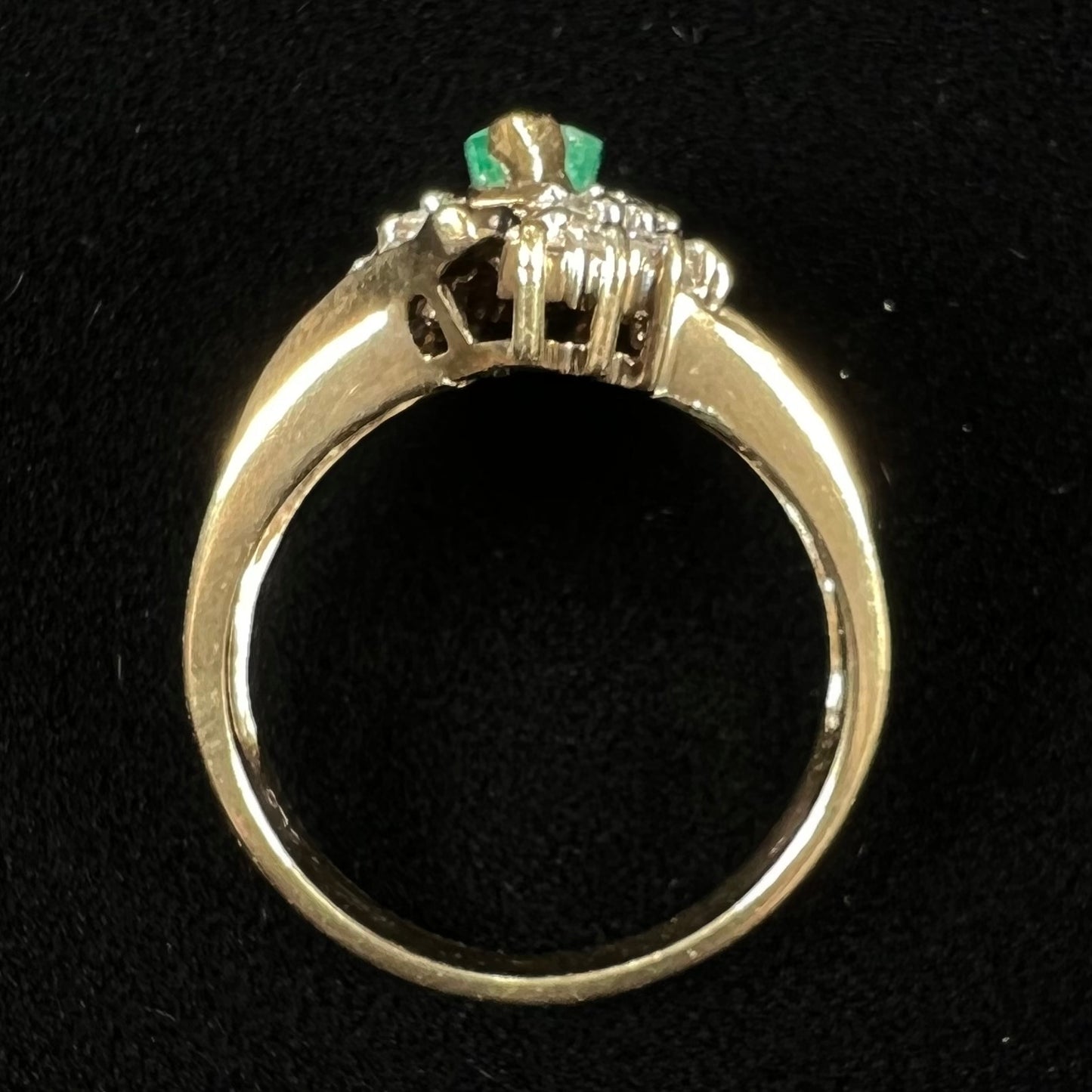 A yellow gold marquise cut emerald and diamond ring.  The diamonds are prong set round cuts and channel set baguette cuts.