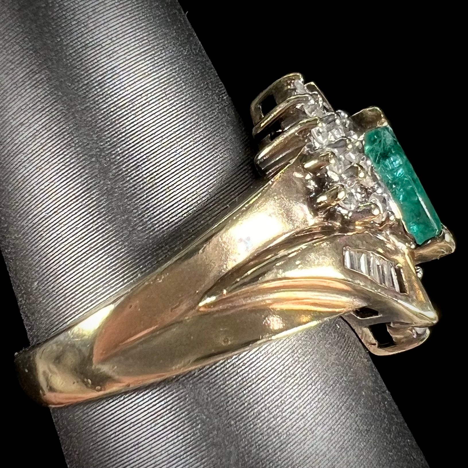 A yellow gold marquise cut emerald and diamond ring.  The diamonds are prong set round cuts and channel set baguette cuts.