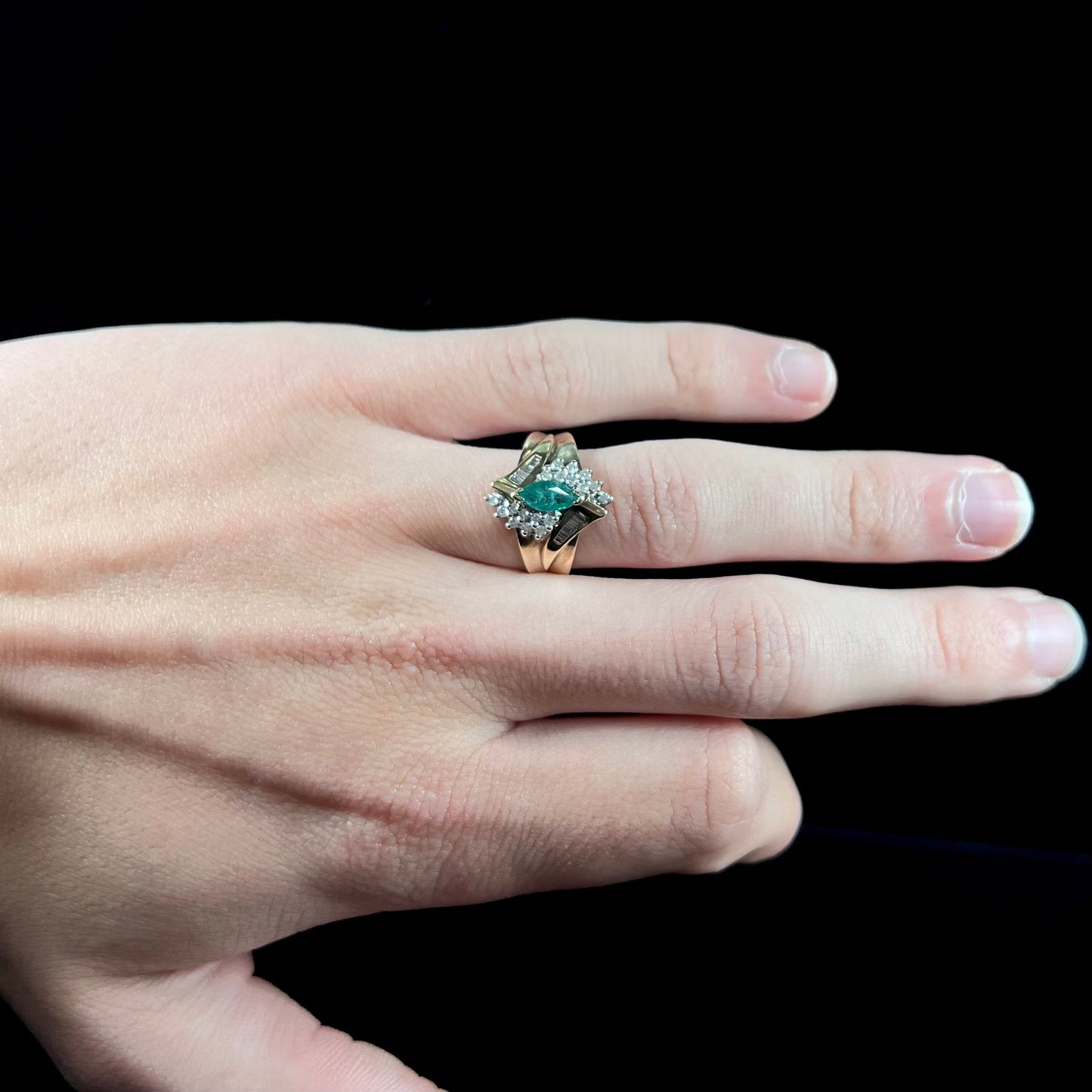 A yellow gold marquise cut emerald and diamond ring.  The diamonds are prong set round cuts and channel set baguette cuts.