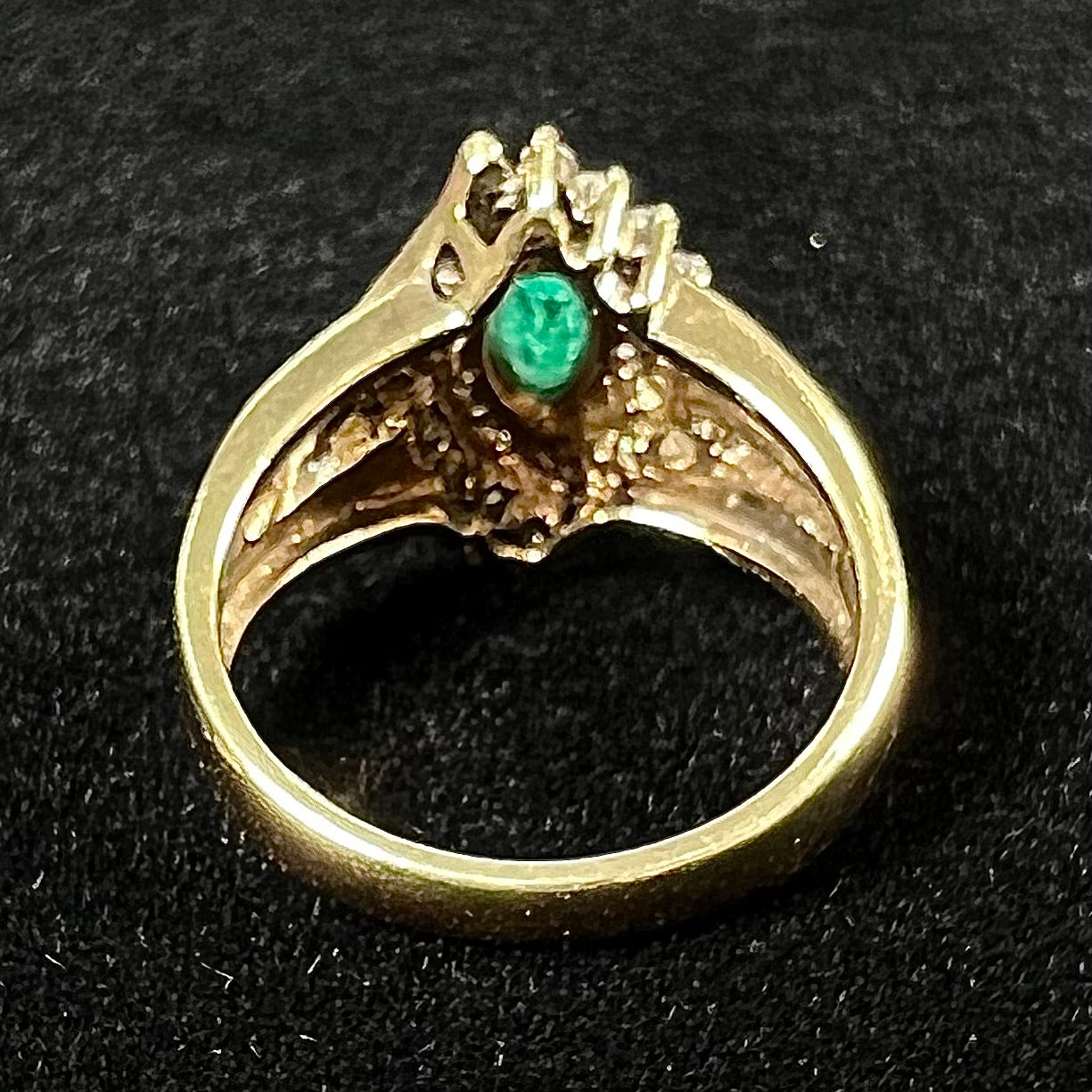 A yellow gold marquise cut emerald and diamond ring.  The diamonds are prong set round cuts and channel set baguette cuts.