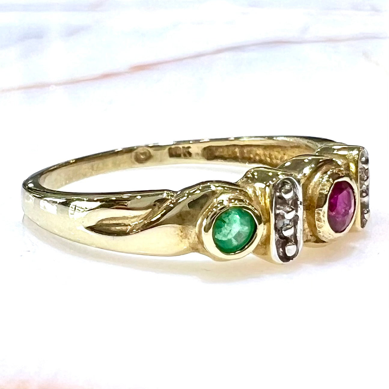 Three stone ring set with blue sapphire, lab created ruby, emerald, and two small diamonds in yellow gold.