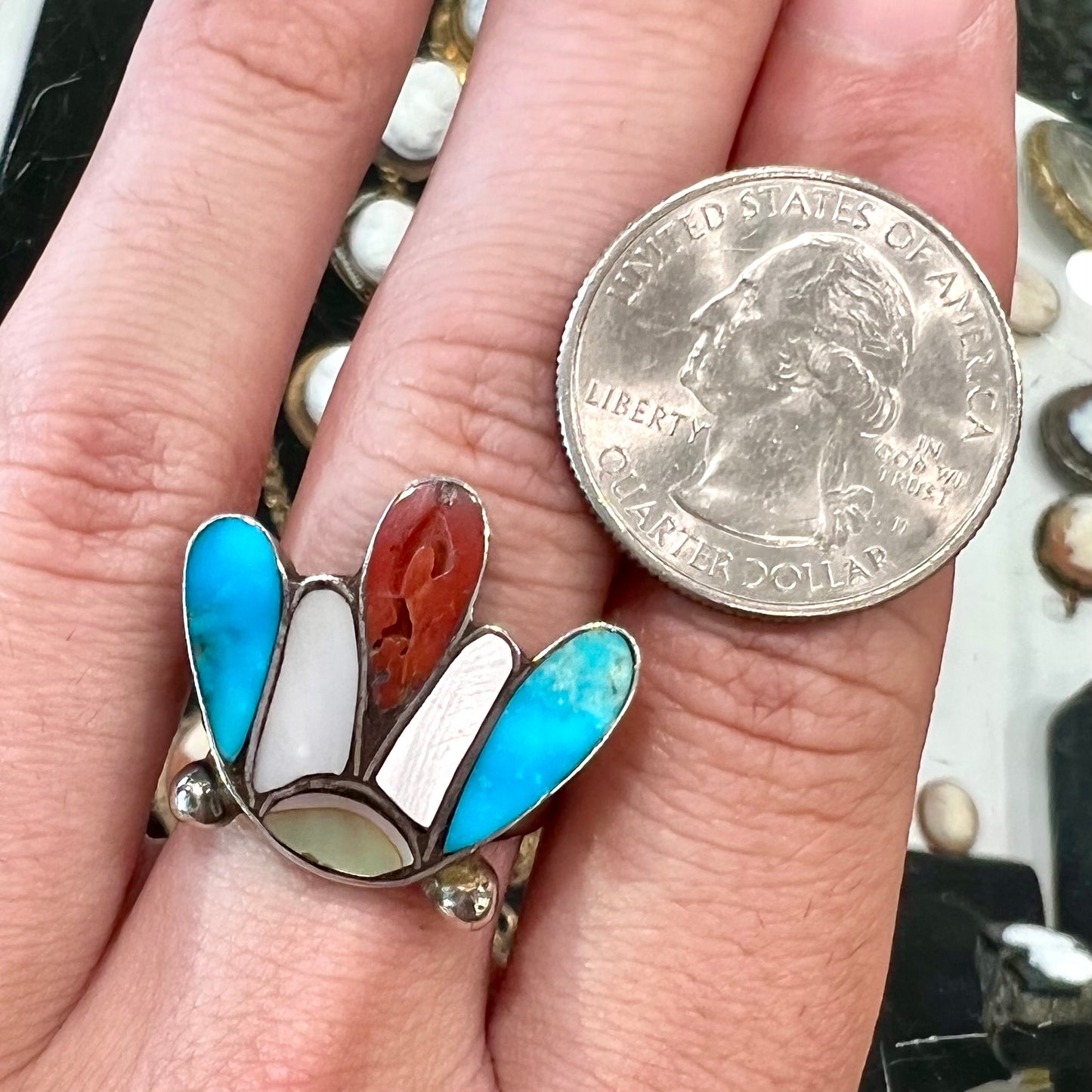 A turquoise, coral, and mother of pearl stone inlay ring made in the motif of a Zuni Indian headdress.