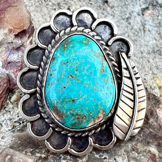 A sterling silver Navajo style ring.  The ring is set with a turquoise stone from Pilot Mountain.  There is a feather decoration next to the stone.