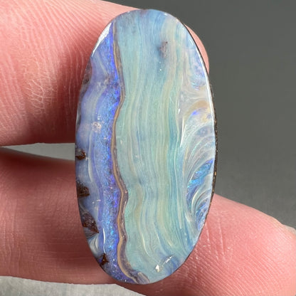 A loose, oval cabochon cut boulder opal stone from Queensland, Australia.