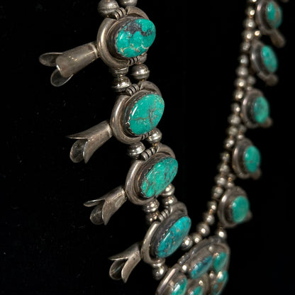 A silver Kingman turquoise squash blossom necklace.  The necklace is made with handmade Navajo pearls.