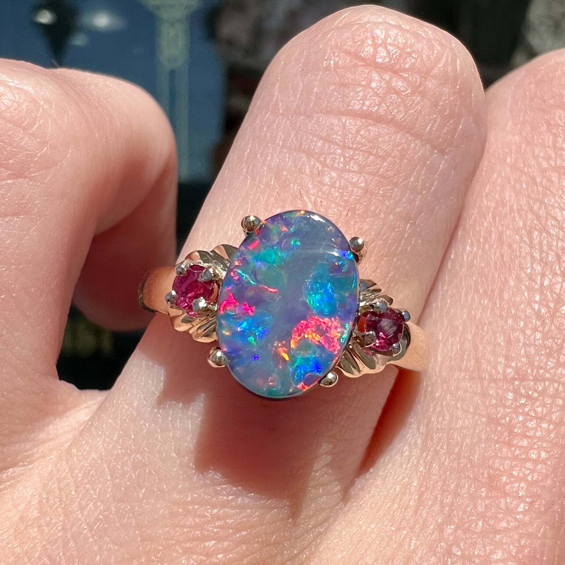 A yellow gold ring prong set with a black opal doublet cabochon and two round ruby accents.