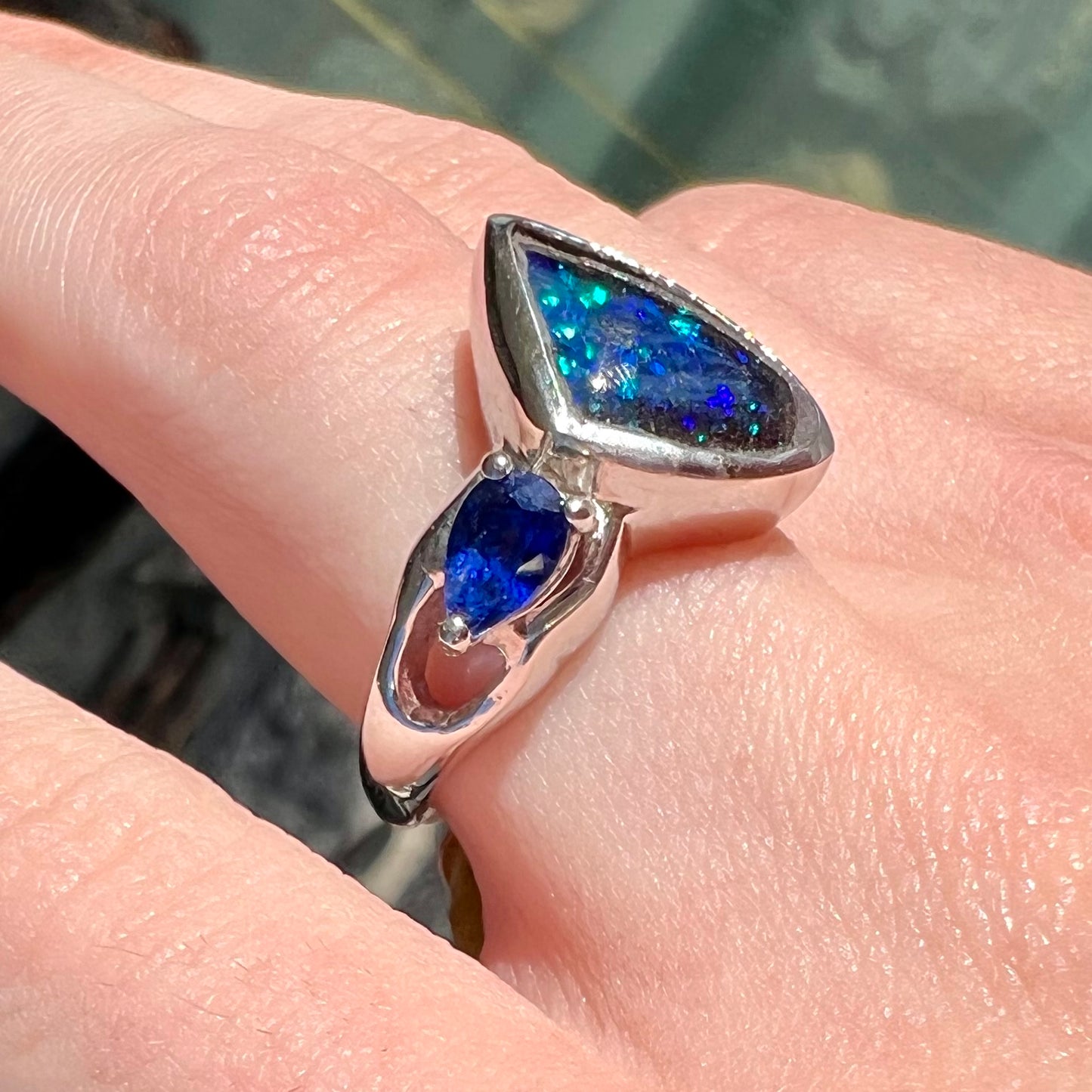 A ladies' white gold ring set with Australian black boulder opal and pear shape blue sapphire.