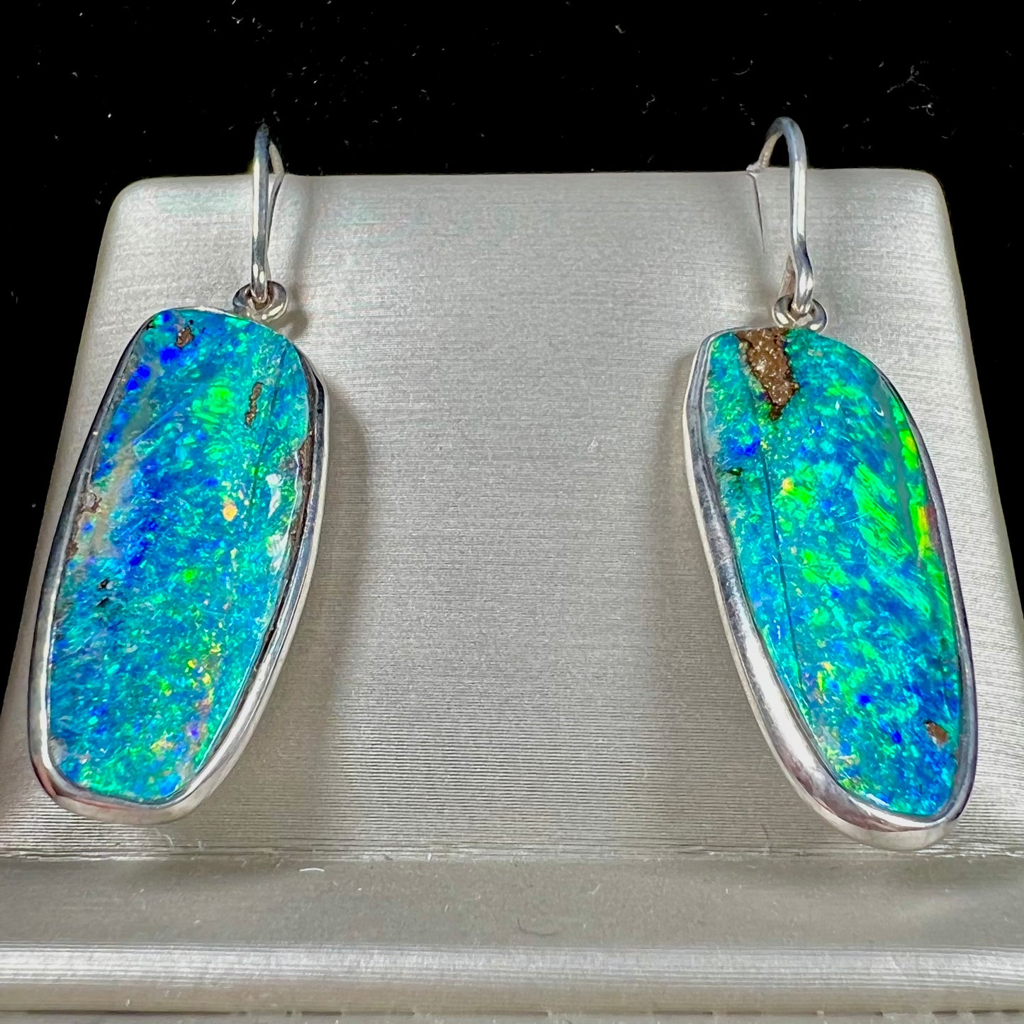 A pair of white gold boulder opal French wire dangle earrings.  The opal is predominantly glimmery blue.