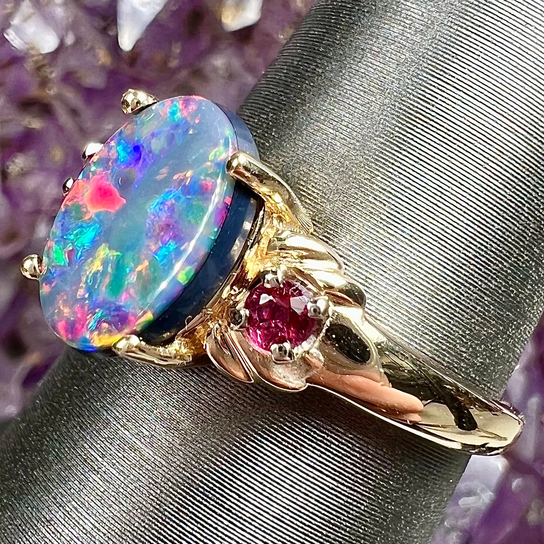 A yellow gold ring prong set with a black opal doublet cabochon and two round ruby accents.