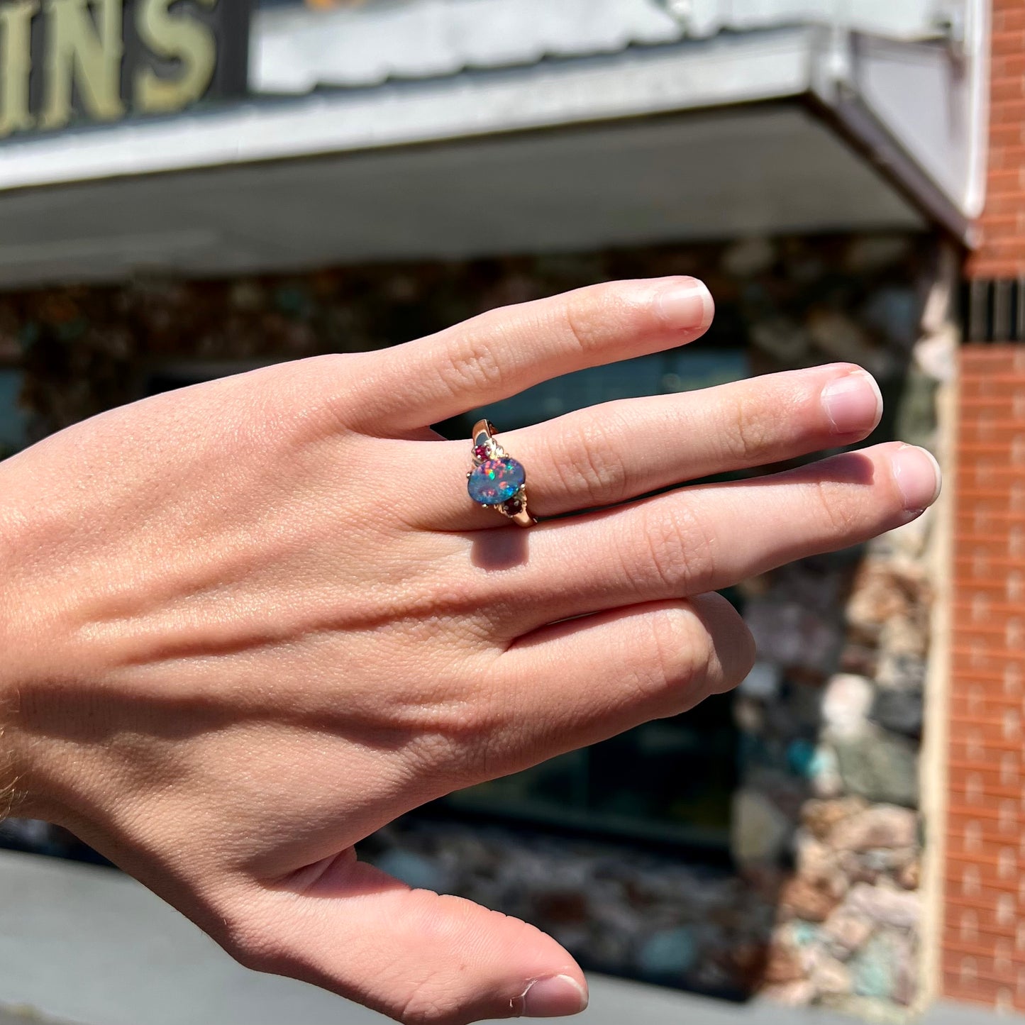 A yellow gold ring prong set with a black opal doublet cabochon and two round ruby accents.