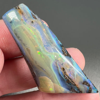 A freeform shaped, polished boulder opal stone from Queensland, Australia.  The stone has red, orange, green, and blue fire.