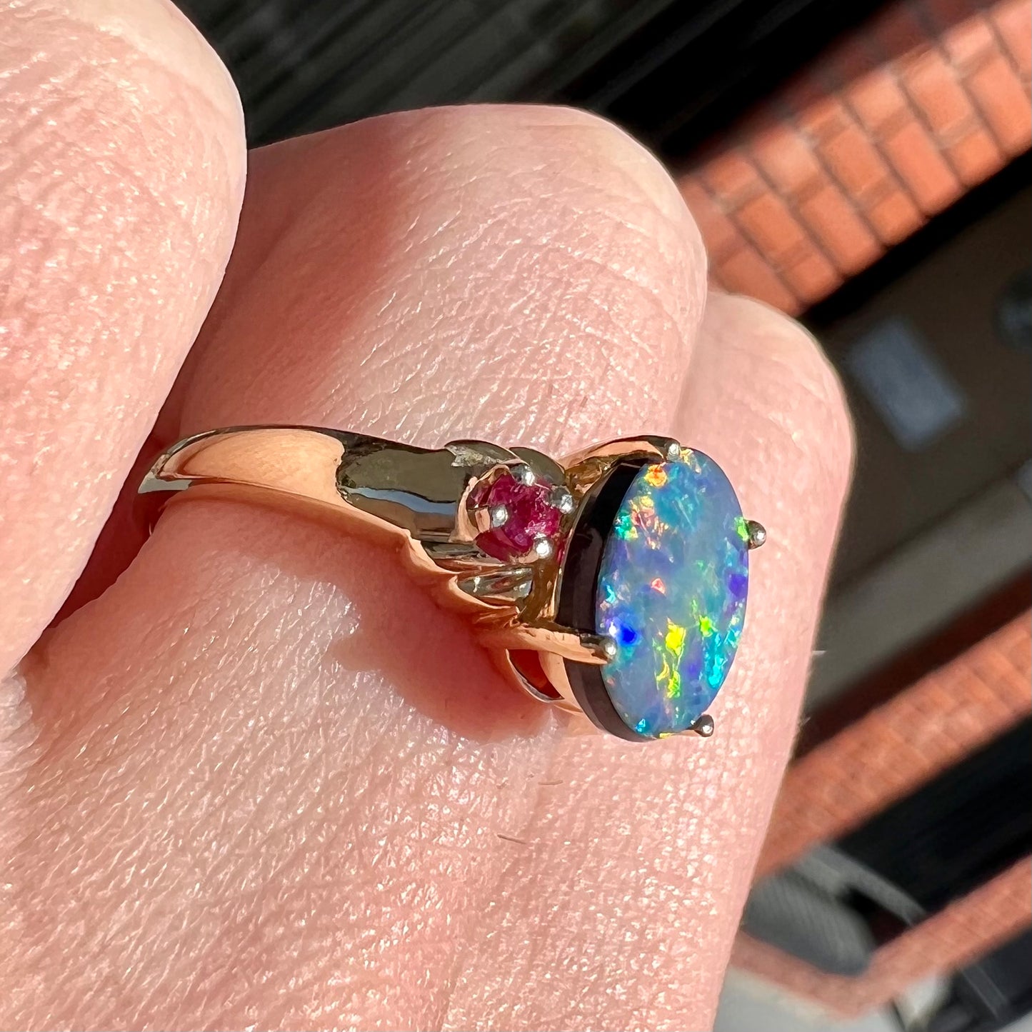 A yellow gold ring prong set with a black opal doublet cabochon and two round ruby accents.