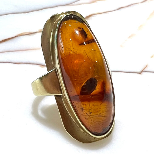 An oval cabochon cut Baltic amber stone set in a yellow gold ring and stamped "AMBER GUILD."