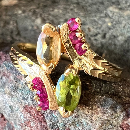 A gold twisted shank ring set with a marquise cut citrine, marquise cut peridot, and round cut ruby accents.