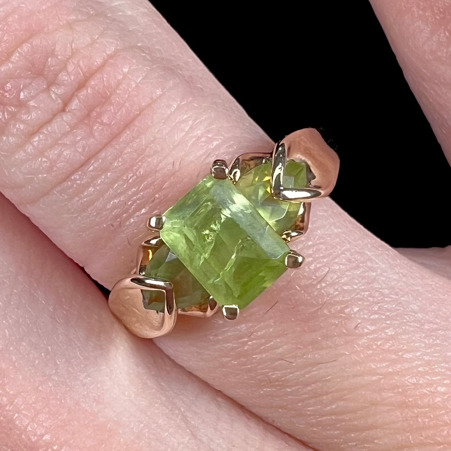 A ladies' three stone peridot ring in yellow gold.  The center stone is emerald cut, and the side stones are pear shaped.