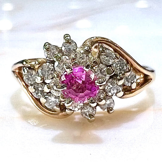 A round pink sapphire high-set in a yellow gold diamond cluster ring.