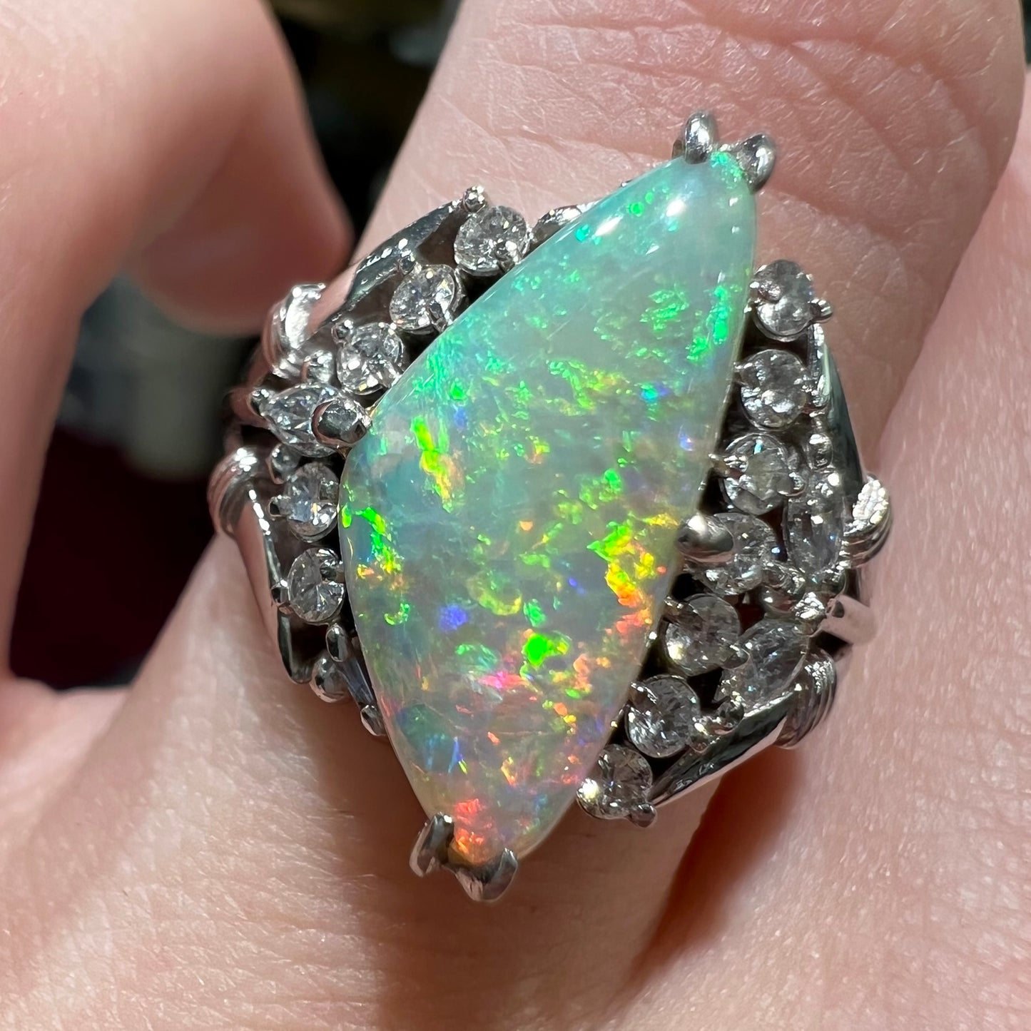 A freeform triangular cabochon cut Lightning Ridge white crystal opal set with diamonds in an ornate platinum split shank setting.