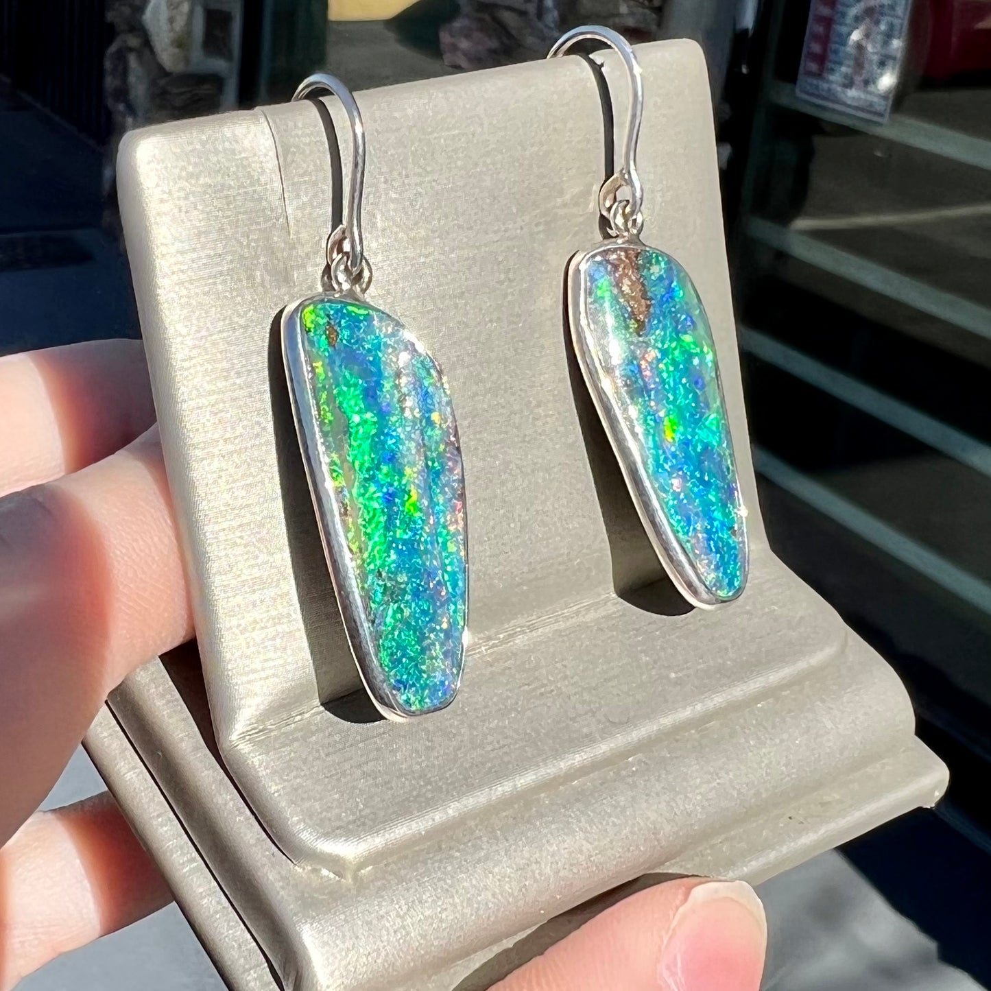 A pair of white gold boulder opal French wire dangle earrings.  The opal is predominantly glimmery blue.