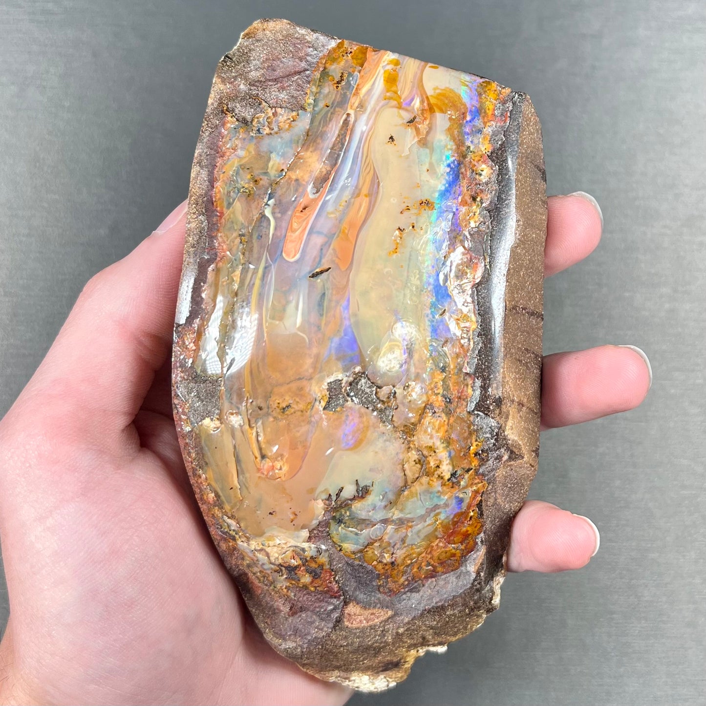 A polished Quilpie boulder opal specimen.  The stone has a stripe of bright blue, green, and purple.