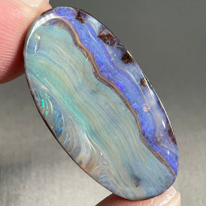 A loose, oval cabochon cut boulder opal stone from Queensland, Australia.