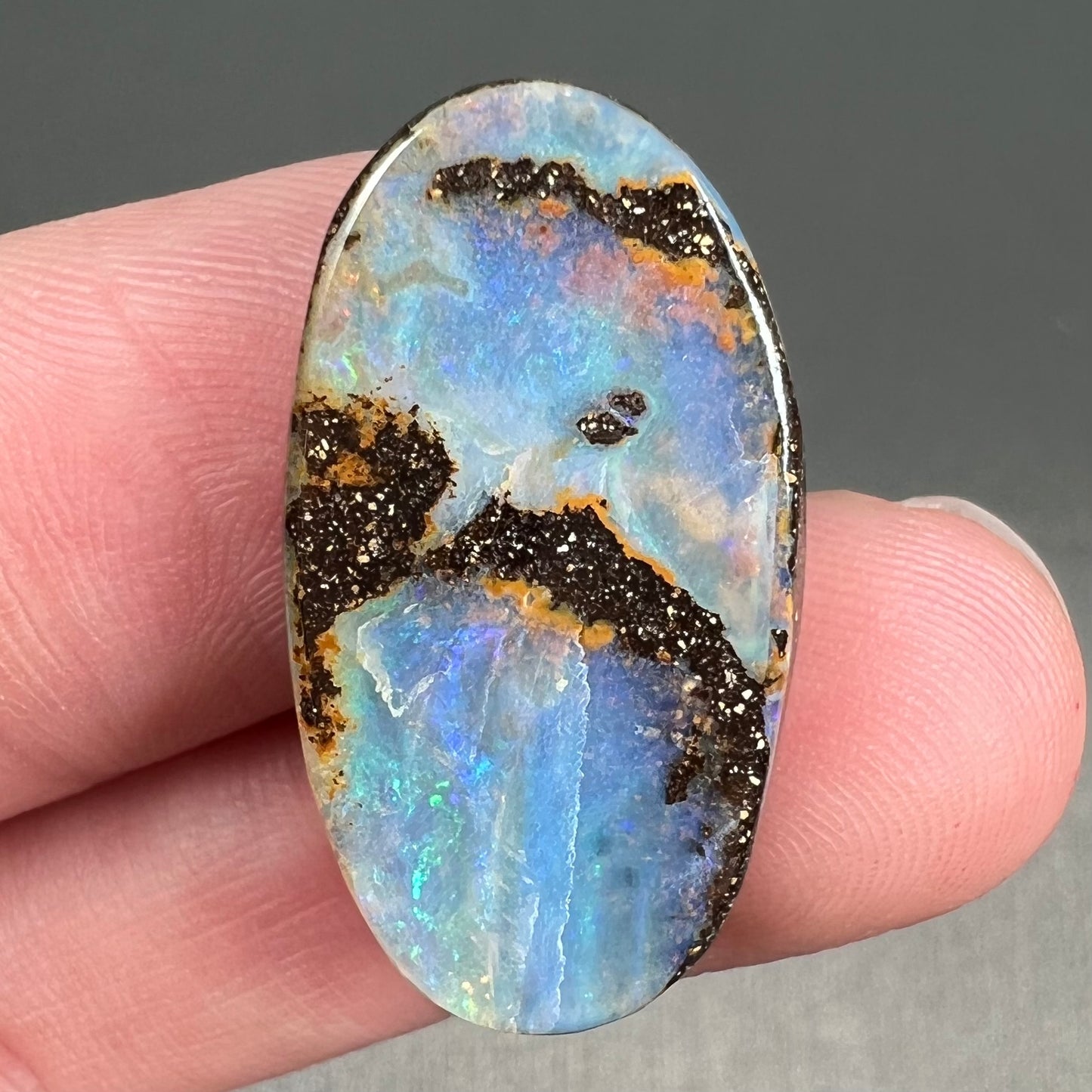 A loose, oval cabochon cut boulder opal stone from Queensland, Australia.