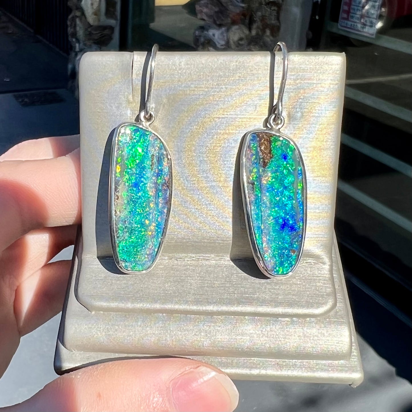 A pair of white gold boulder opal French wire dangle earrings.  The opal is predominantly glimmery blue.