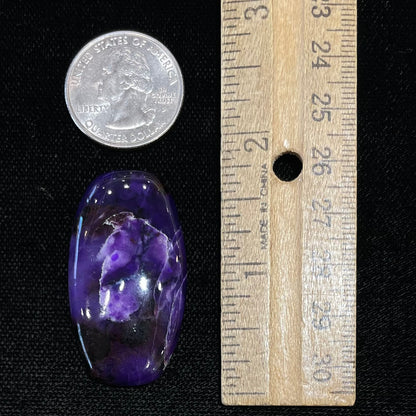 A loose, barrel cabochon cut purple sugilite stone.