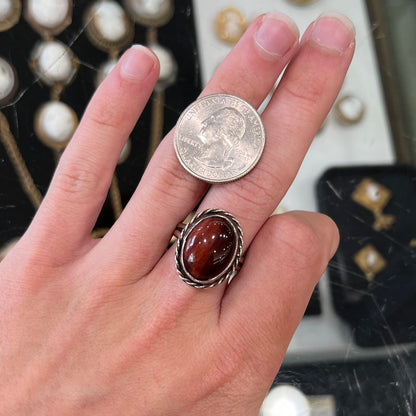 A men's sterling silver rope bezel ring set with a red tiger's eye stone.