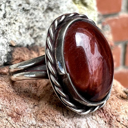 A men's sterling silver rope bezel ring set with a red tiger's eye stone.