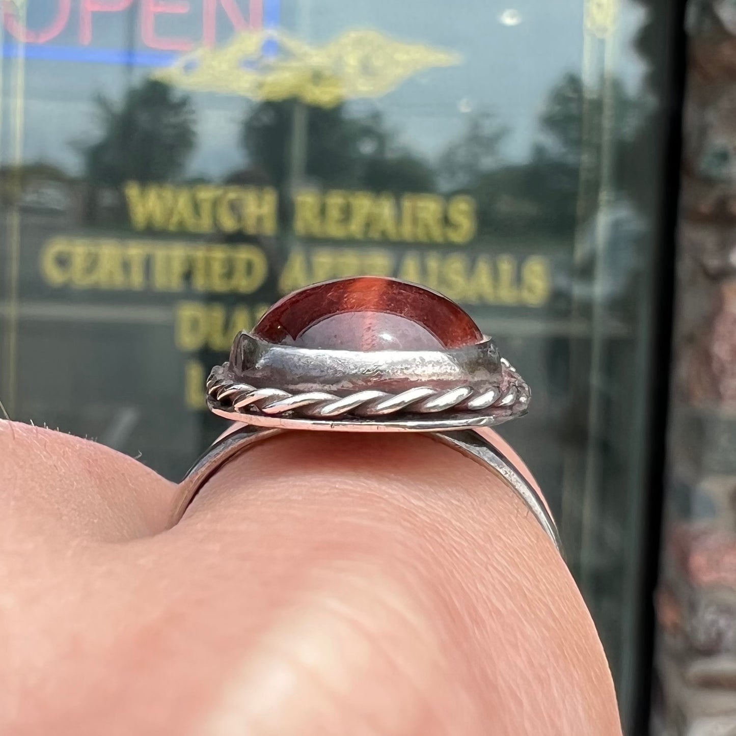 A men's sterling silver rope bezel ring set with a red tiger's eye stone.