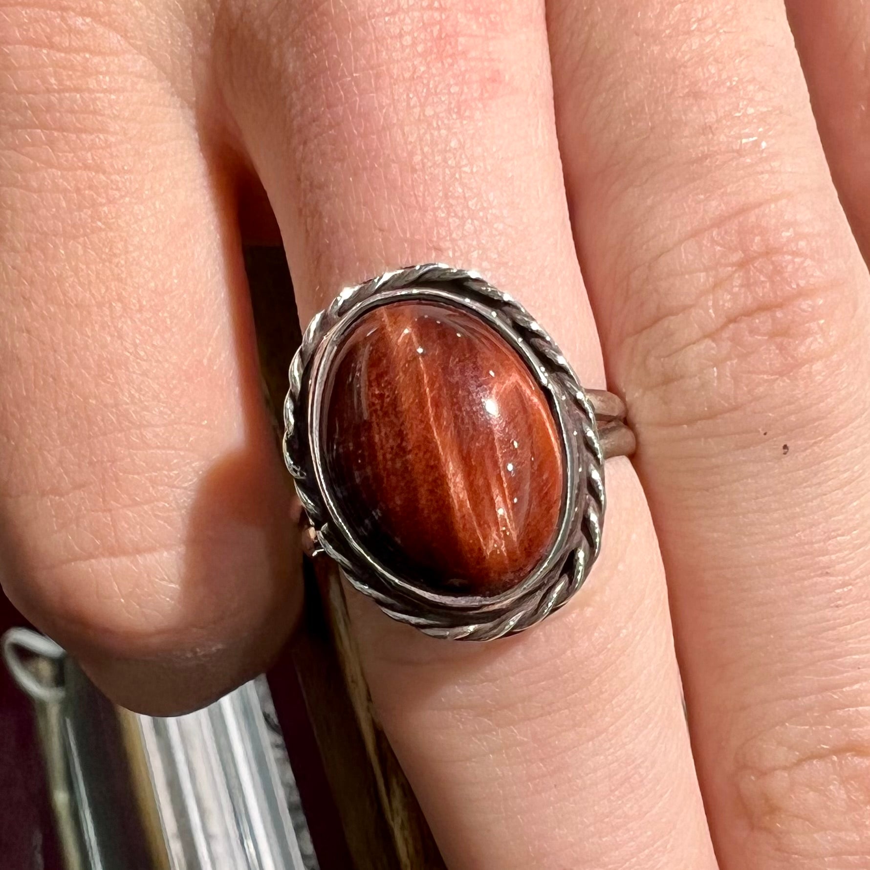 A men's sterling silver rope bezel ring set with a red tiger's eye stone.