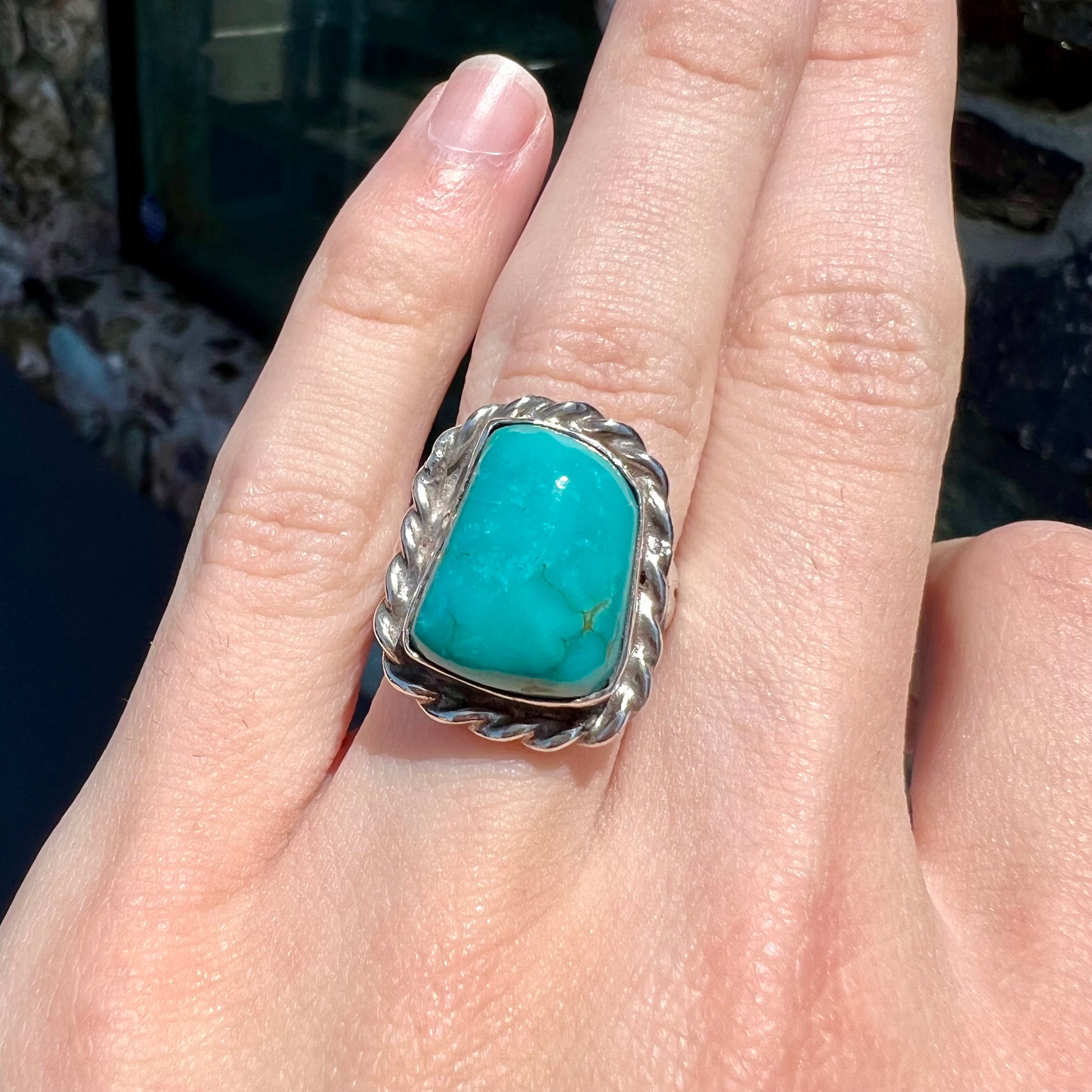 A sterling silver turquoise split shank ring.  There is a handmade silver rope around the turquoise.