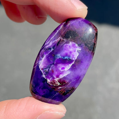 A loose, barrel cabochon cut purple sugilite stone.