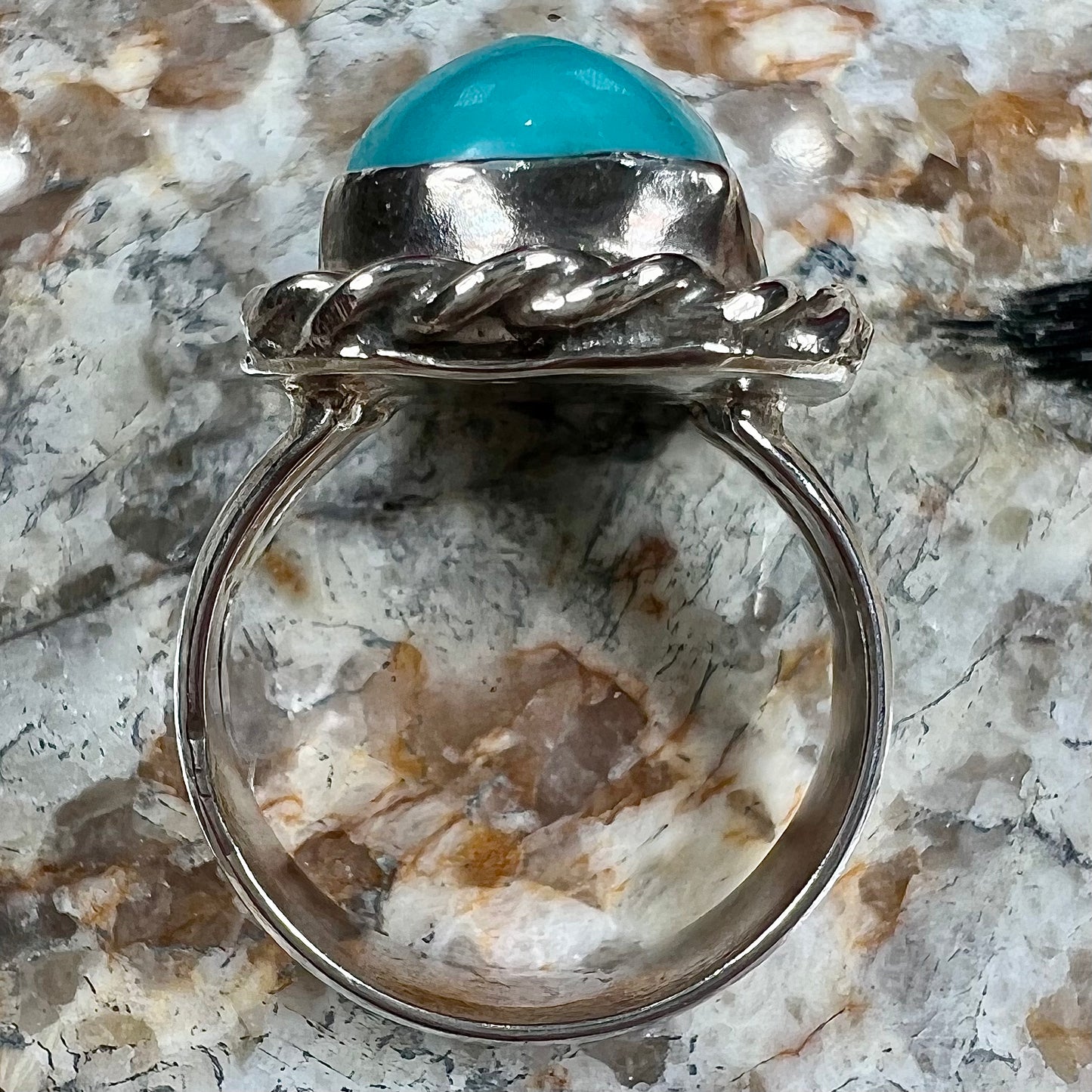 A sterling silver turquoise split shank ring.  There is a handmade silver rope around the turquoise.