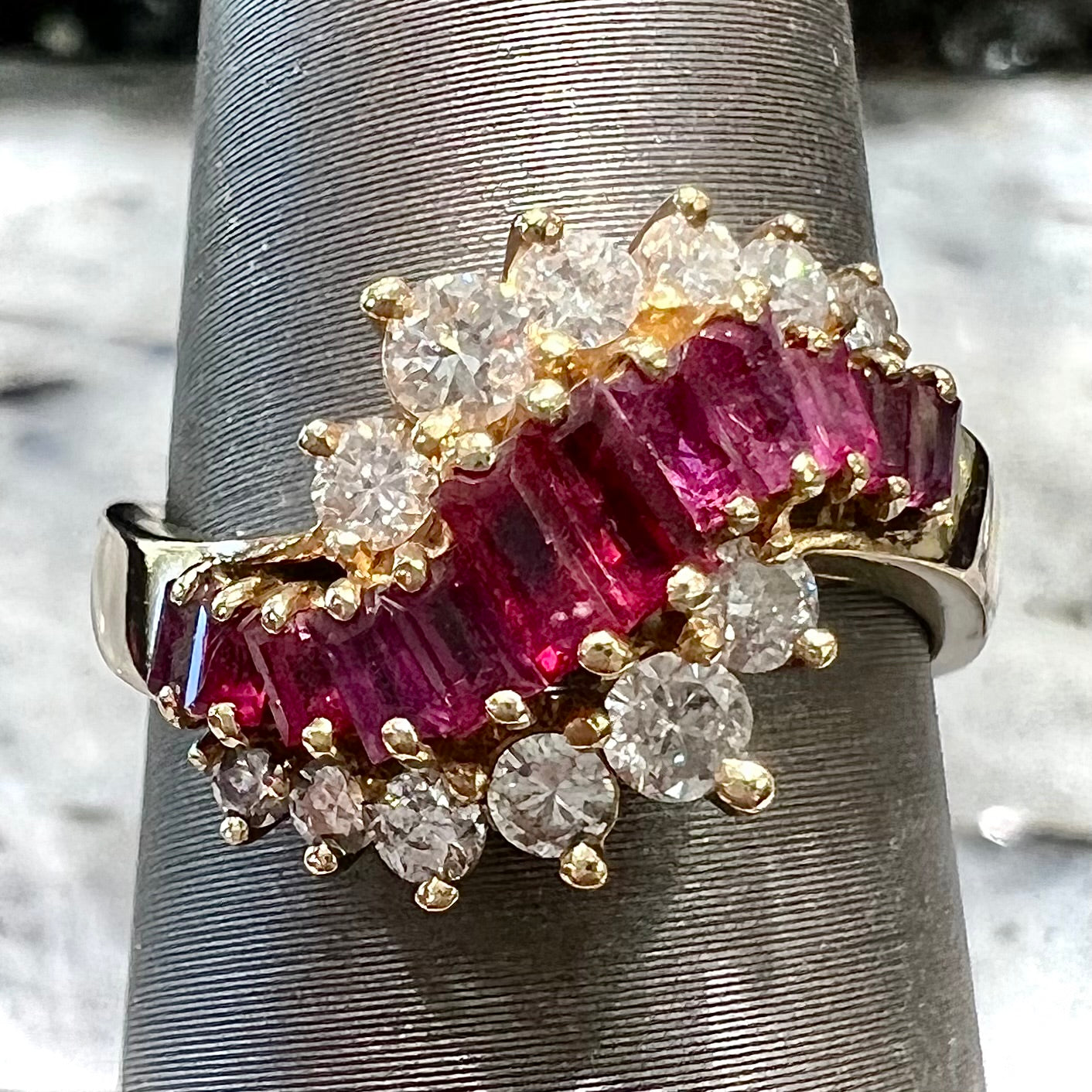 A yellow gold ladies' ring set with 12 baguette cut rubies and 12 Standard Round Brilliant Cut diamonds.