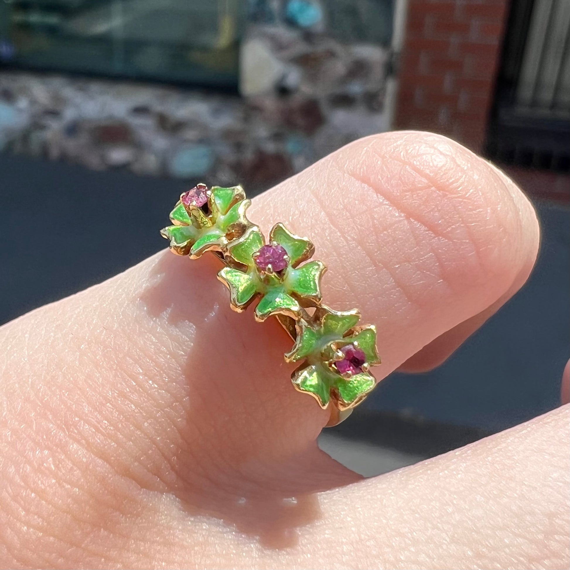 A gold ladies' ring in the motif of three flowers set with round ruby centers and green enameled petals.