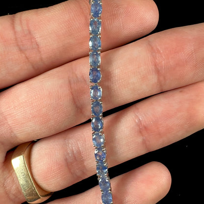 A sterling silver tennis bracelet set with faceted oval cut blue sapphires.