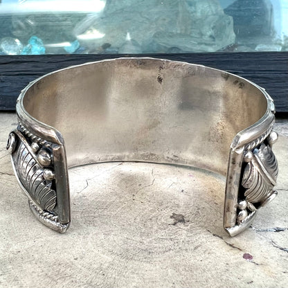 An ornate men's sterling silver turquoise cuff bracelet.  There are three turquoise stones set with silver feathers.