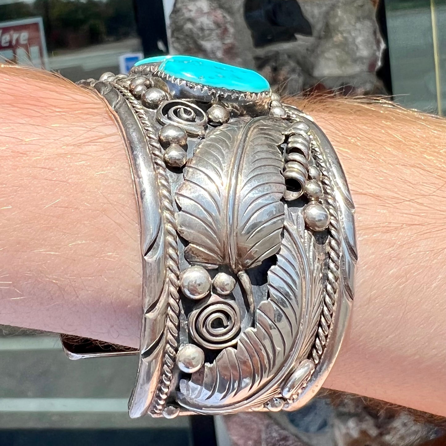 An ornate men's sterling silver turquoise cuff bracelet.  There are three turquoise stones set with silver feathers.