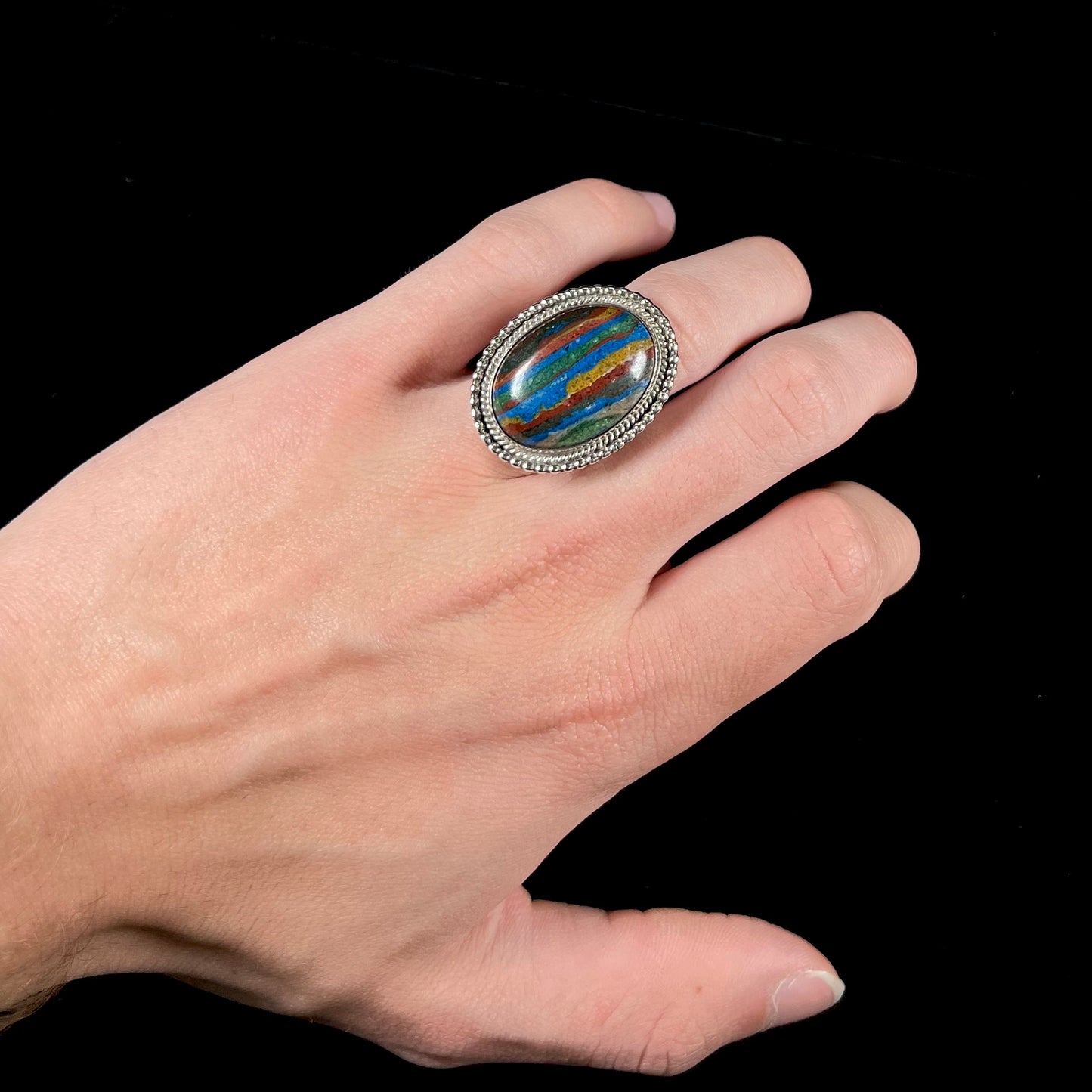 A split shank, rope bezel set silver ring set with an oval cut fordite paint stone.