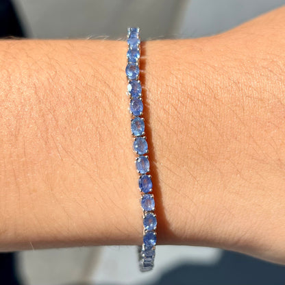 A sterling silver tennis bracelet set with faceted oval cut blue sapphires.