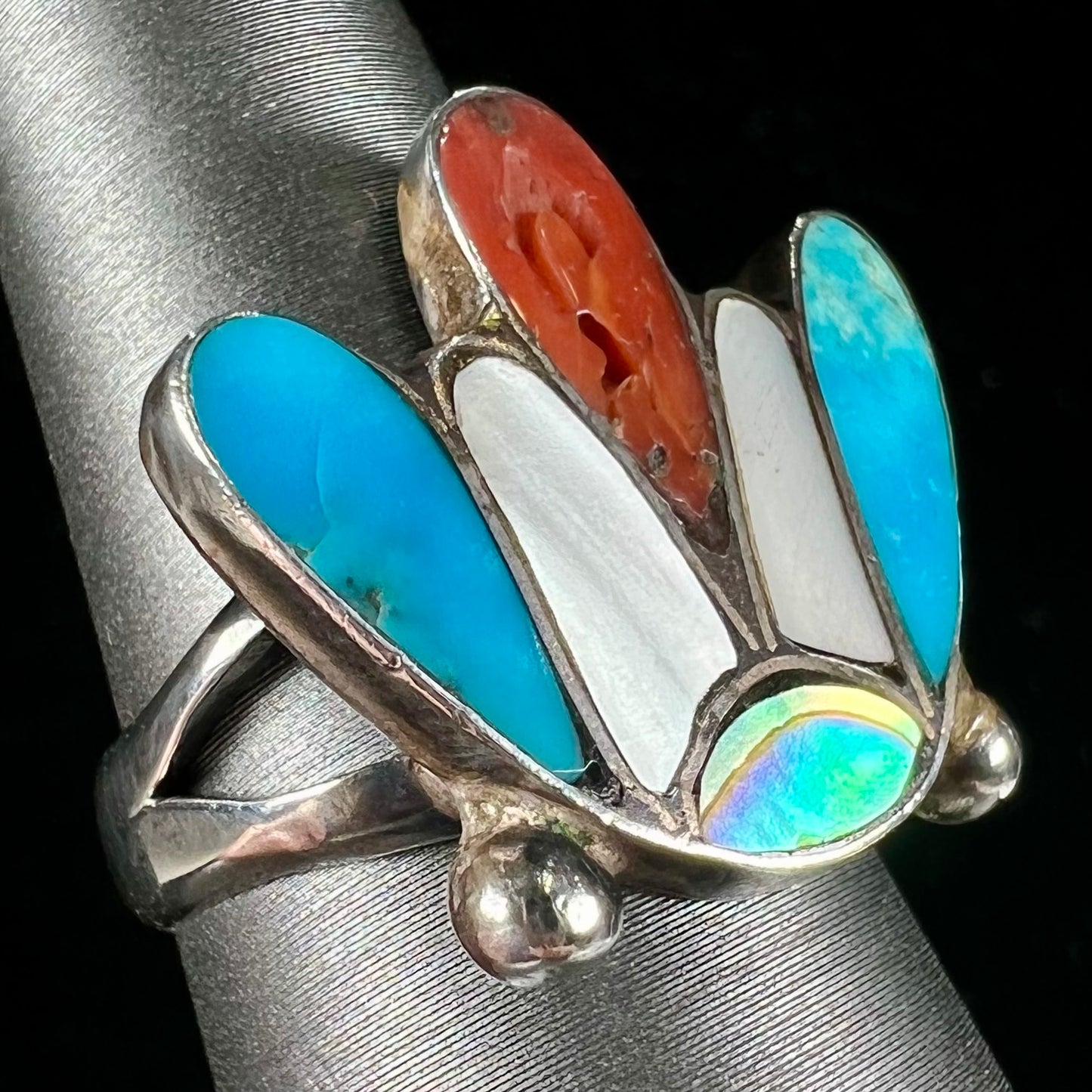 A turquoise, coral, and mother of pearl stone inlay ring made in the motif of a Zuni Indian headdress.