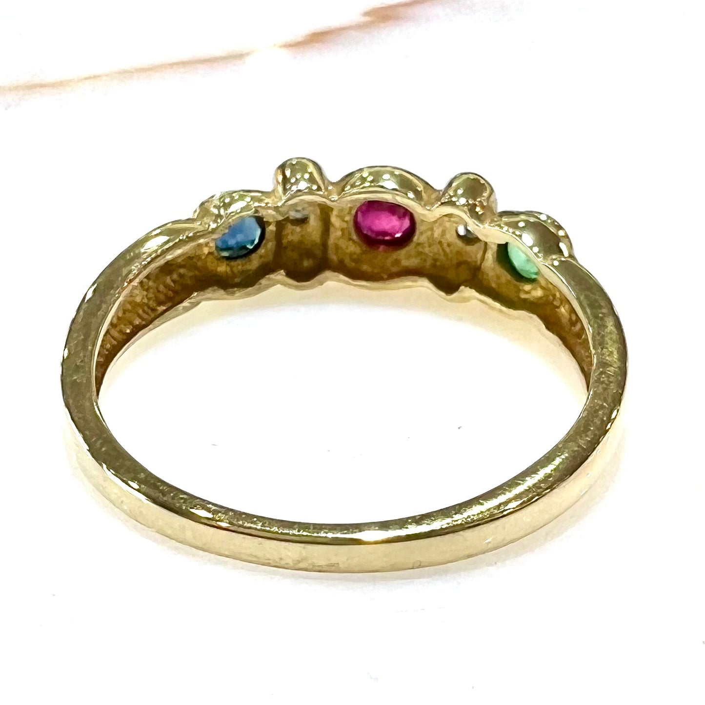 Three stone ring set with blue sapphire, lab created ruby, emerald, and two small diamonds in yellow gold.