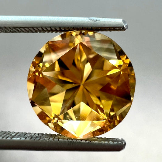 A loose, faceted round cut citrine stone with back facets that form a five pointed star.