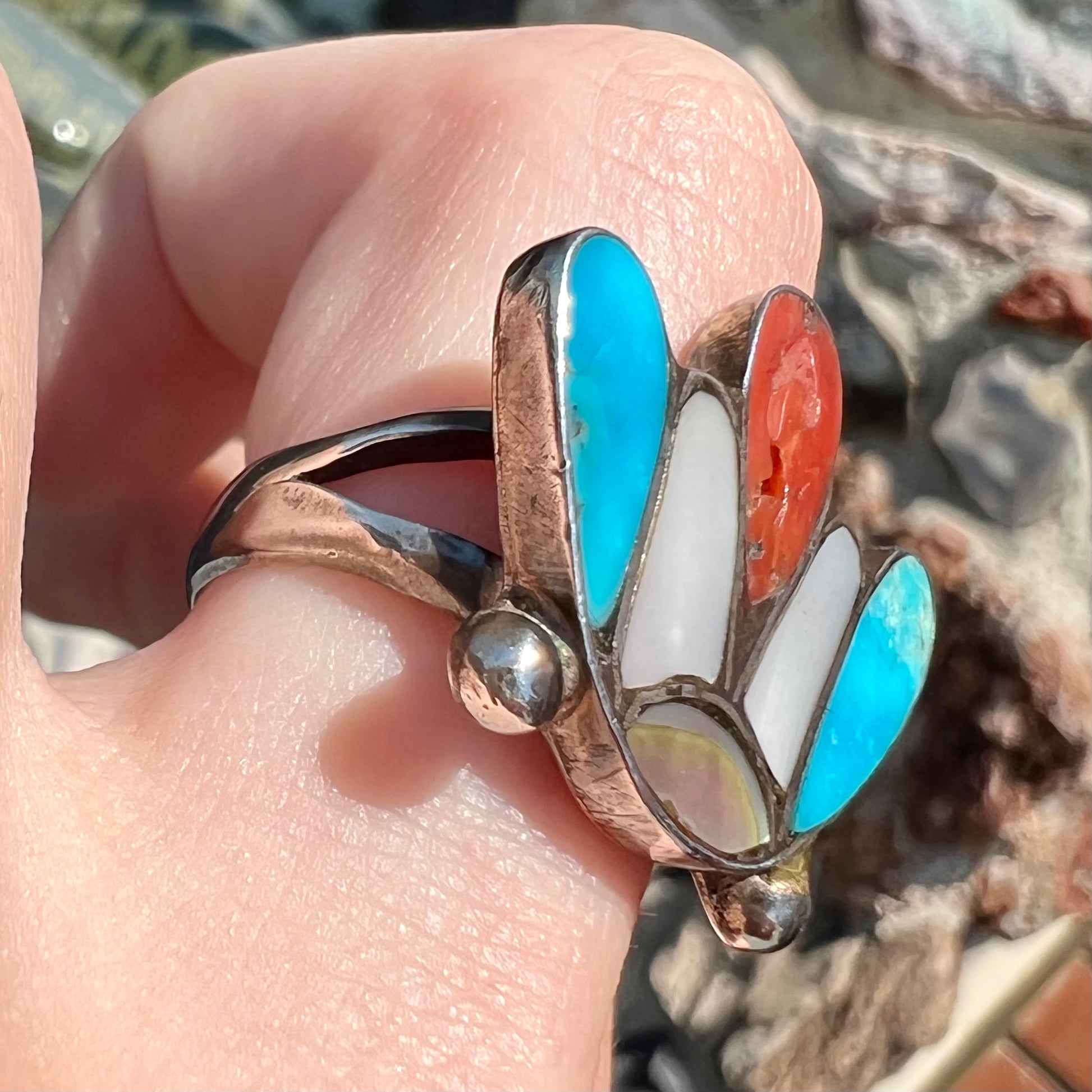 A turquoise, coral, and mother of pearl stone inlay ring made in the motif of a Zuni Indian headdress.