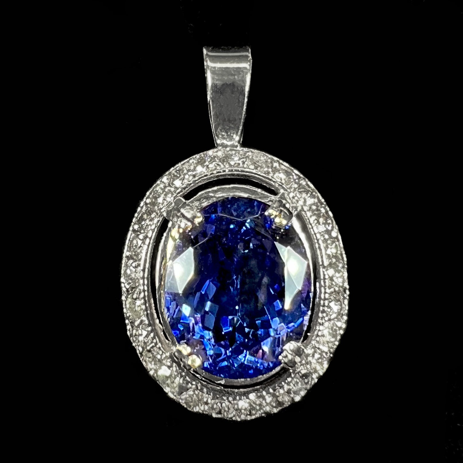 A ladies' 14kt white gold tanzanite and diamond halo pendant.  The sides of the pendant have filigree.