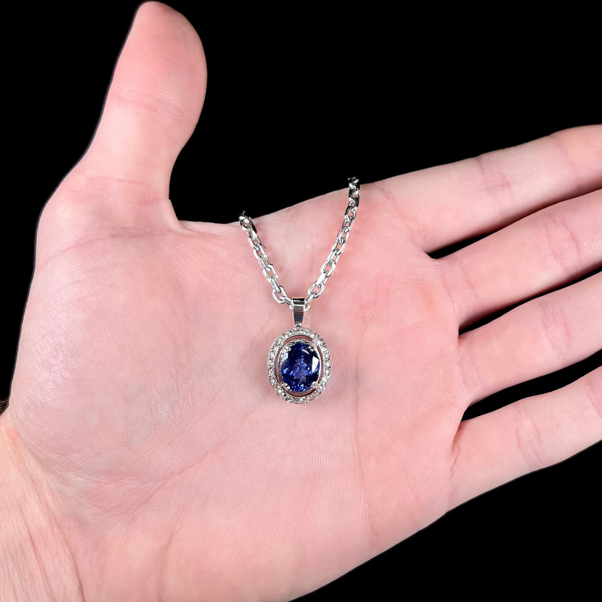 A ladies' 14kt white gold tanzanite and diamond halo pendant.  The sides of the pendant have filigree.