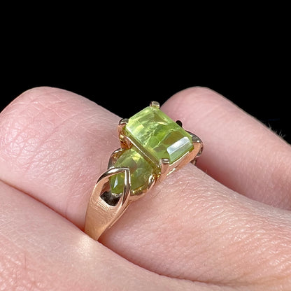 A ladies' three stone peridot ring in yellow gold.  The center stone is emerald cut, and the side stones are pear shaped.